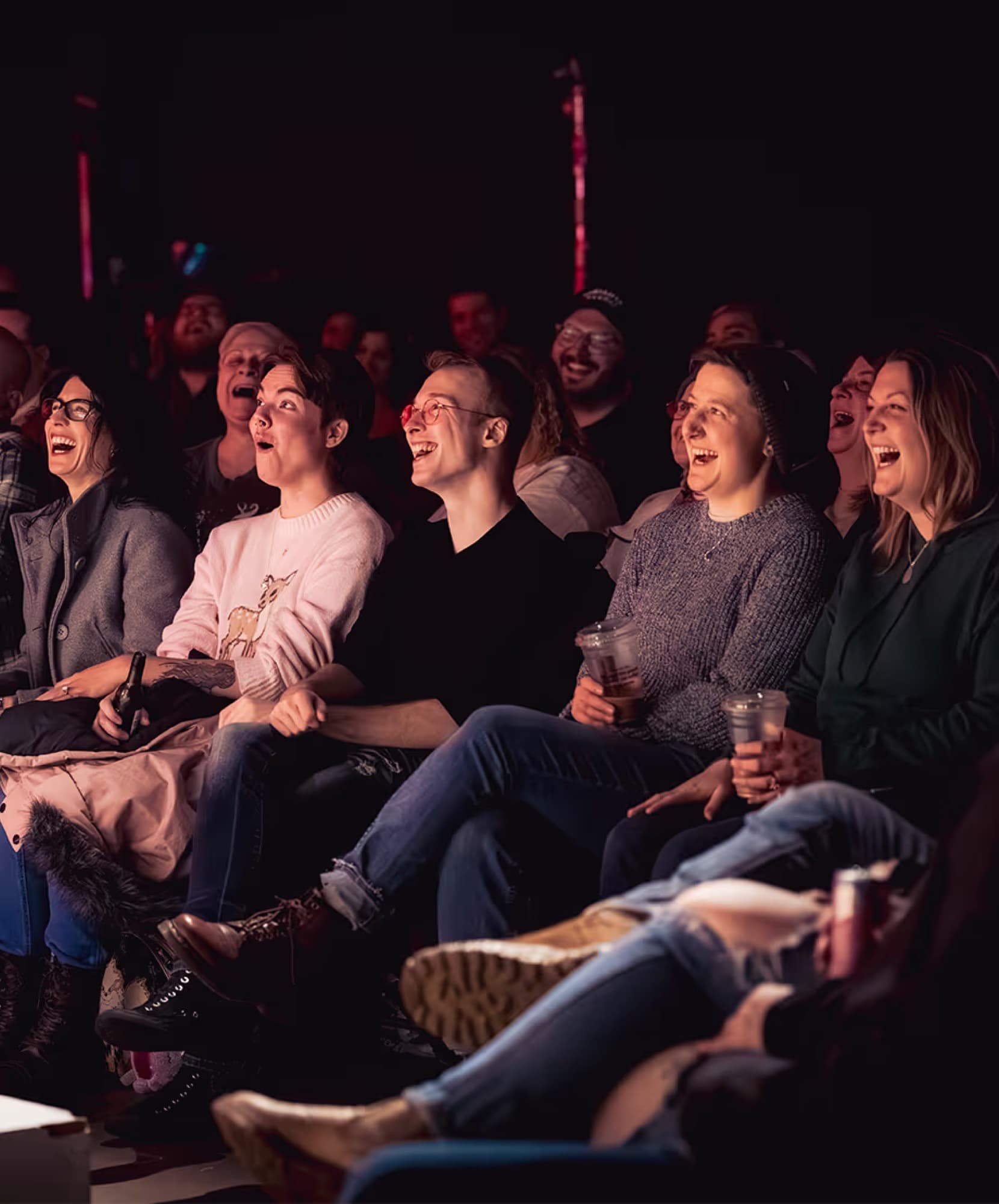 A packed basement room lit warm from the stage, drinks on every table.