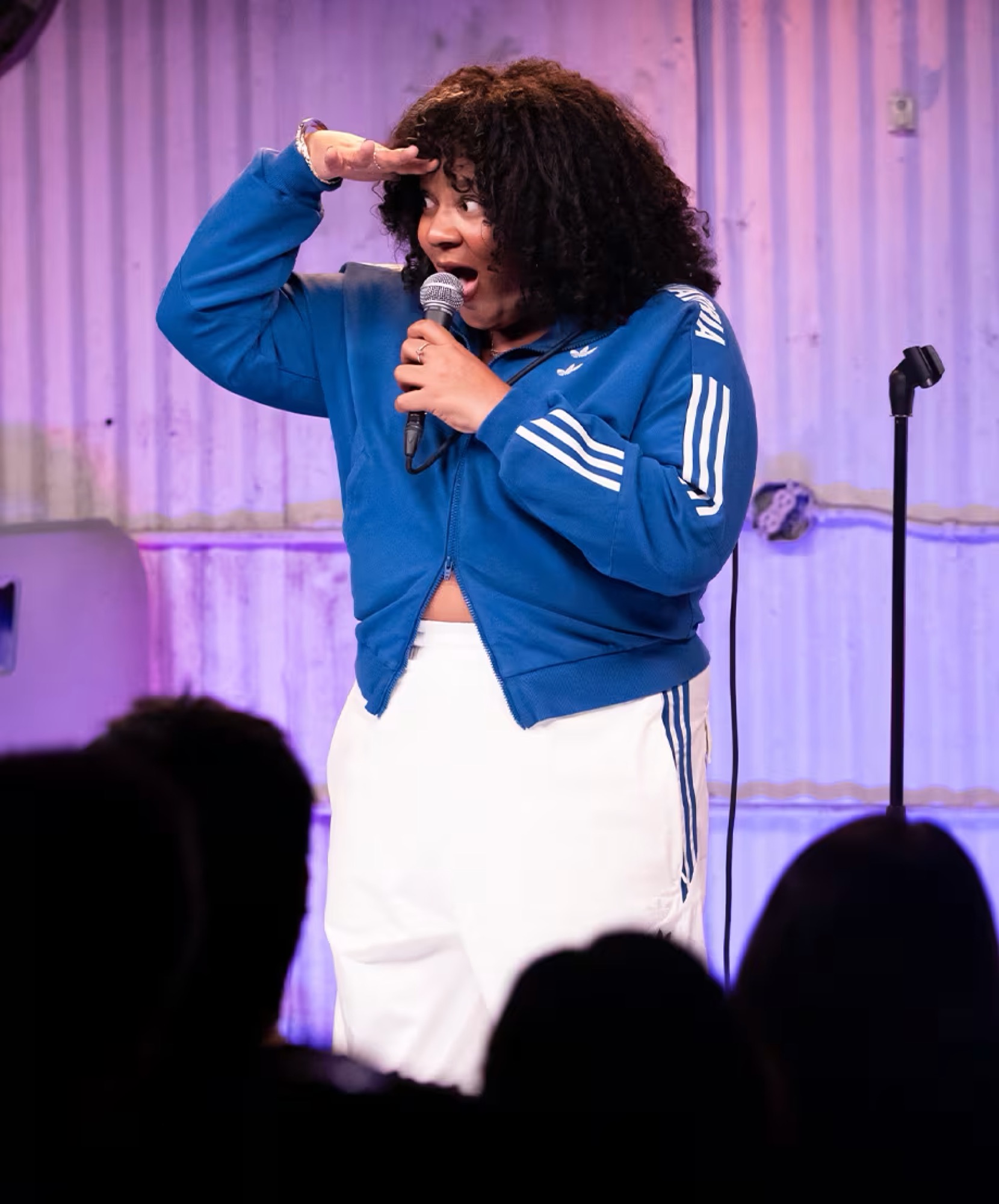 A comic mid-punchline under a purple stage wash.