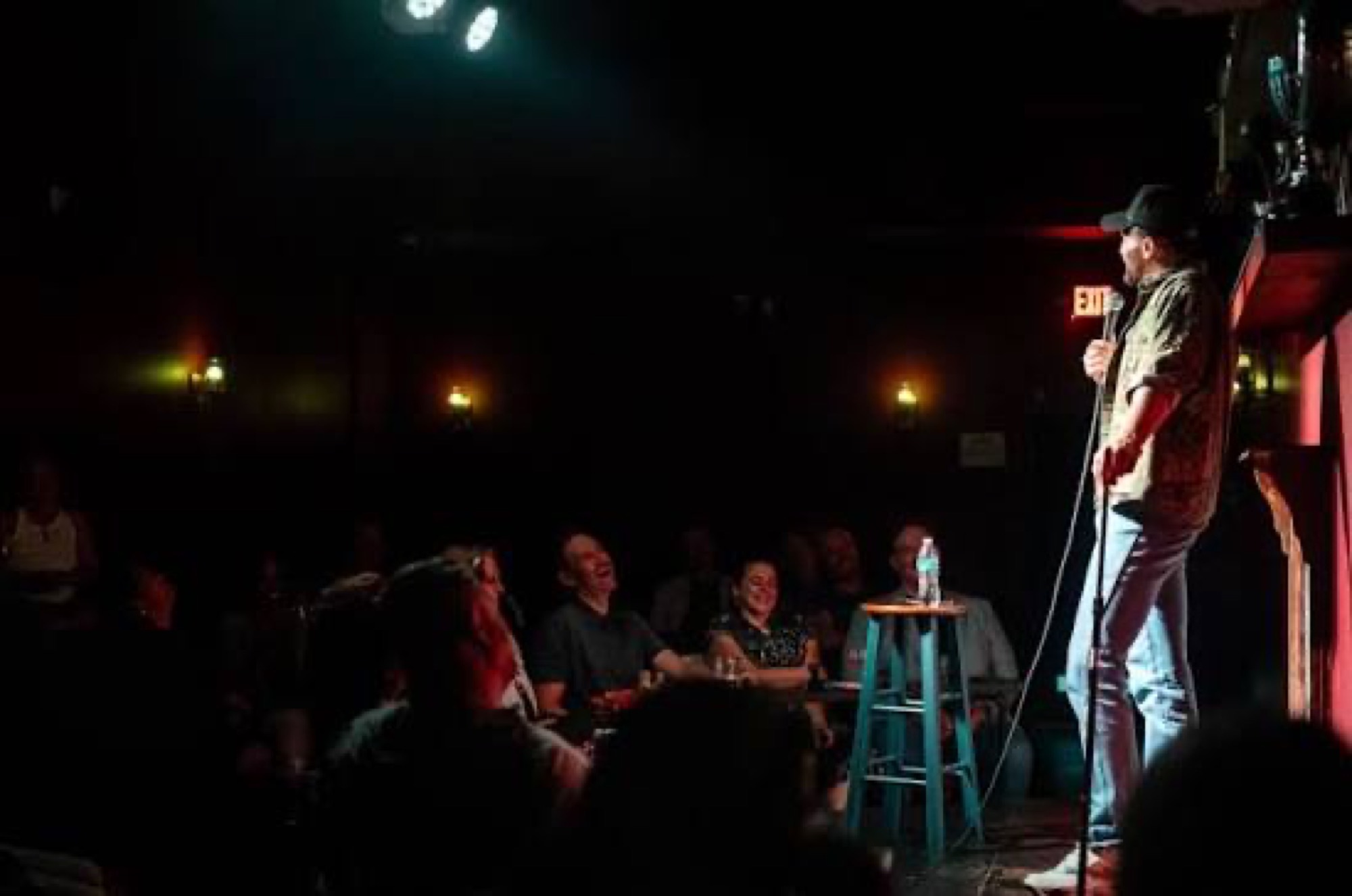 A comic on a small stage facing a seated crowd.